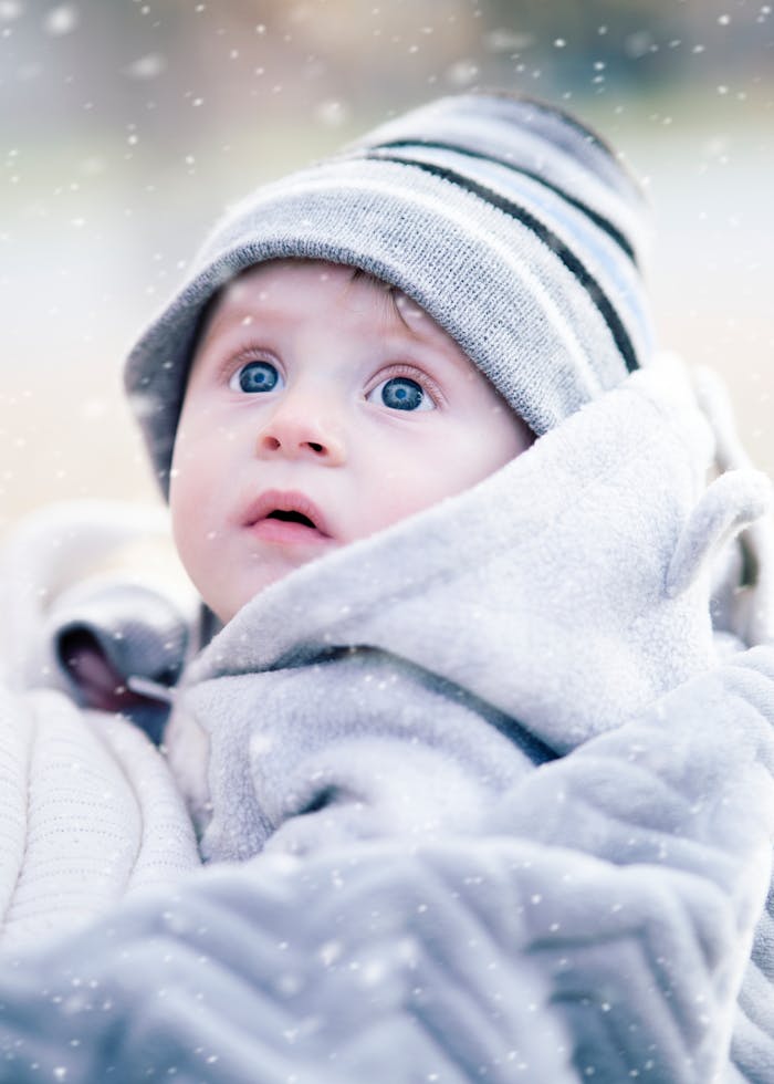 our-story Cute baby wrapped in a blanket with a knit hat, gazing upward during snowfall.